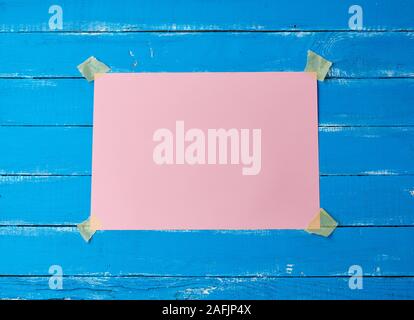 Collée avec du ruban adhésif un vide rectangulaire feuille de papier rose sur un fond de bois bleu, place pour une inscription Banque D'Images