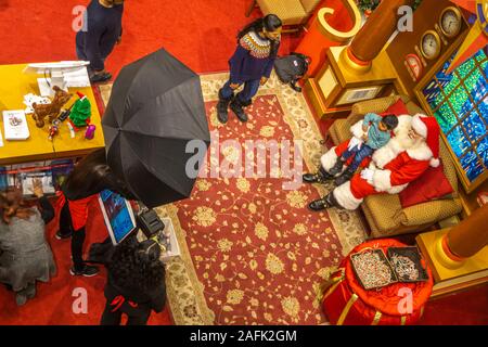 Centre-ville de Scarborough, Toronto, Canada, décembre 2019 - Le Père Noël est titulaire d'un enfant sur ses genoux pour une photo souvenir pendant que les parents regardent Banque D'Images