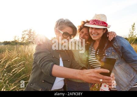 Groupe d'amis de sexe féminin marche à travers champ sur Camping Selfies qui pose pour Banque D'Images