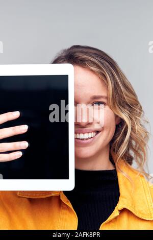 Studio Portrait Of Smiling Young Woman Covering Face With Digital Tablet Banque D'Images