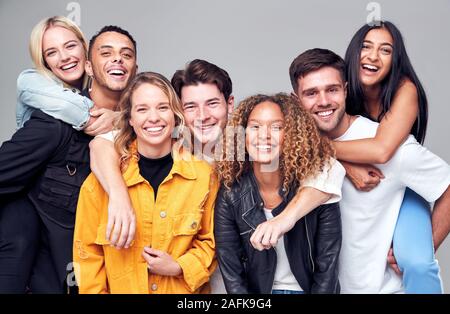 De groupe Multi-Cultural amis donnant à chaque autre Piggybacks And Smiling at Camera Banque D'Images
