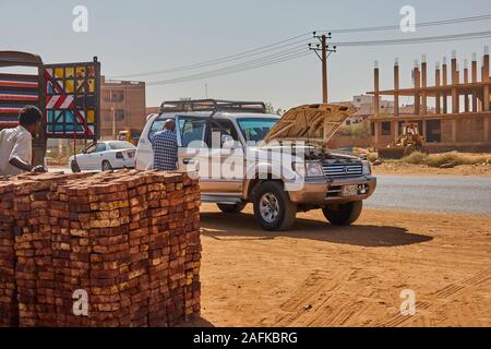 Khartoum, Soudan, ca. Le 8 février, 2019. : véhicule hors route en cas de défaillance d'un moteur à la route en face d'un tas de briques d'argile dans une banlieue de Khar Banque D'Images