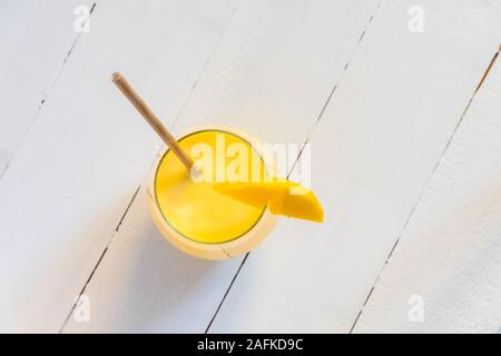 Vue de dessus de boisson traditionnelle indienne lassi à la mangue avec du papier paille et mango coupe sur table en bois blanc Banque D'Images