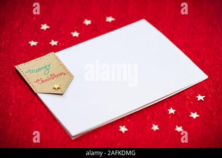 Joyeux Noël écrit sur un papier blanc ou une carte sur fond texturé rouge décorée avec du papier fait de minuscules étoiles blanches. Concept pour Noël Banque D'Images