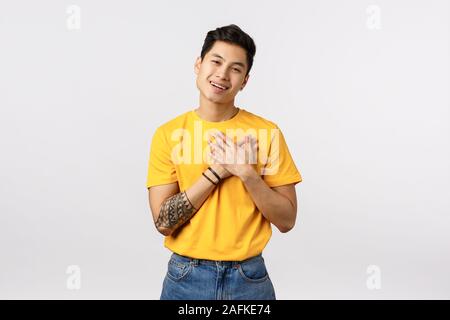 Belle, touché asiatique avec des tatouages en t-shirt jaune, appuyez sur mains à coeur, soupirant avec affection ou l'admiration, smiling, reconnaissant pour remercier Banque D'Images