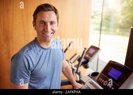 Portrait de l'homme exercice sur tapis roulant à la maison portant des écouteurs sans fil Banque D'Images