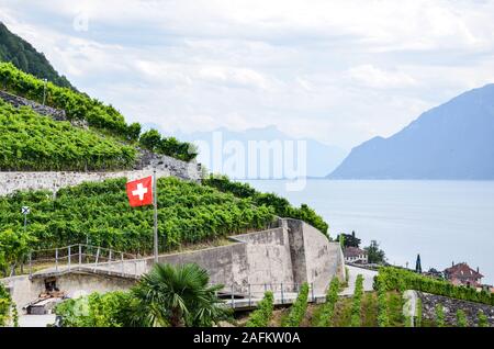 Beaux vignobles en terrasses sur les pentes par le lac de Genève en Suisse photographié sur l'image. En agitant drapeau suisse dans les vignobles. Silhouettes des collines dans l'arrière-plan. Banque D'Images