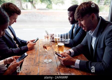 Groupe de collègues d'affaires tous les téléphones mobiles de contrôle tout en répondant pour verre au bar Banque D'Images