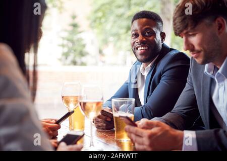 Groupe de collègues d'affaires tous les téléphones mobiles de contrôle tout en répondant pour verre au bar Banque D'Images