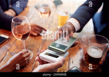 Close Up of Businessman Paying for Round de boissons dans un bar à l'aide de l'App sur téléphone mobile sans contact Banque D'Images