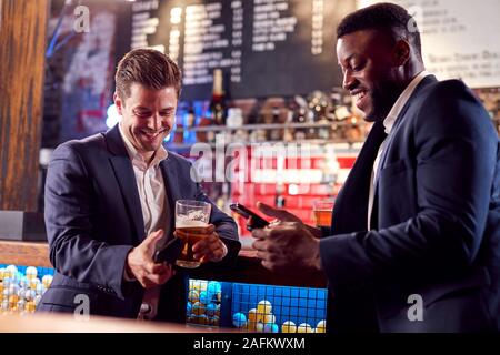 Deux hommes d'contrôler les téléphones mobiles tout en répondant pour verre au bar Banque D'Images