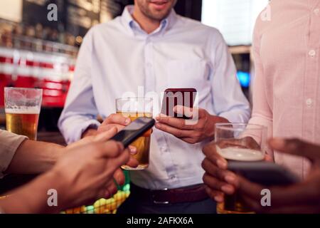 Groupe d'amis tous les téléphones mobiles de contrôle tout en répondant pour verre au bar Banque D'Images