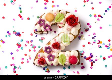 Numéro deux gâteau décoré avec des fleurs, des macarons et confettis isolé sur fond blanc. Copy space Banque D'Images