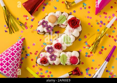 Numéro deux gâteau décoré avec des fleurs, des macarons et confettis isolé sur fond jaune. Copy space Banque D'Images