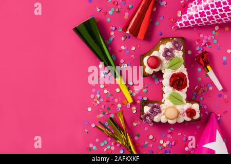 Le numéro un gâteau décoré de fleurs et de cookies sur fond rose. Copy space Banque D'Images