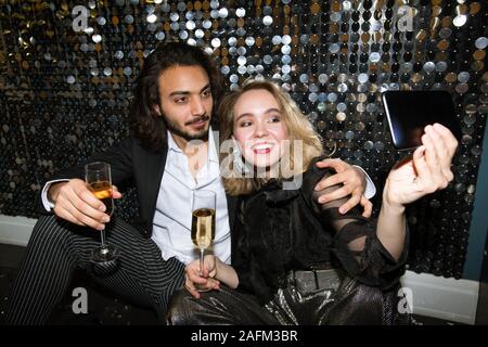 Young affectionate couple en tenue glamour de décisions par selfies mur scintillant Banque D'Images