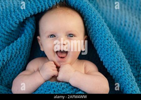 Une happy laughing baby enveloppé dans une couverture bllue Banque D'Images