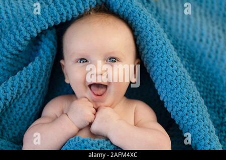 Une happy laughing baby enveloppé dans une couverture bllue Banque D'Images