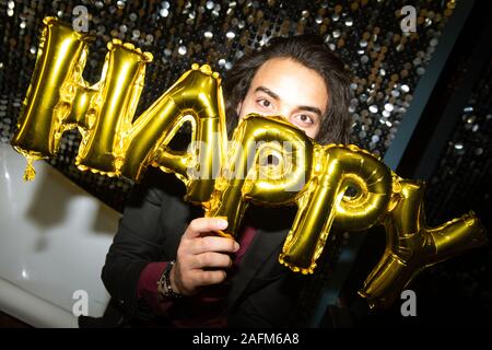 Jeune brunette holding golden ballon gonflable lettres par son visage Banque D'Images