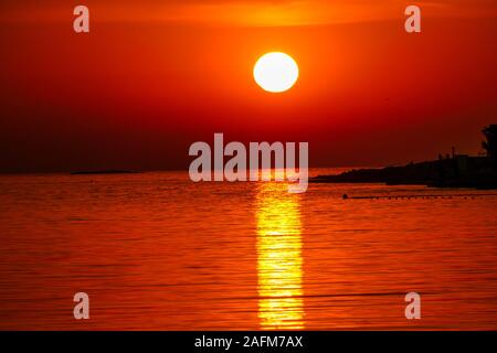 Coucher de soleil romantique par une plage. Le soleil se couche sur l'horizon. Les rayons de soleil se reflétant dans les eaux de la mer calme. Il y a une île sur le côté. Peu d'oiseaux Banque D'Images