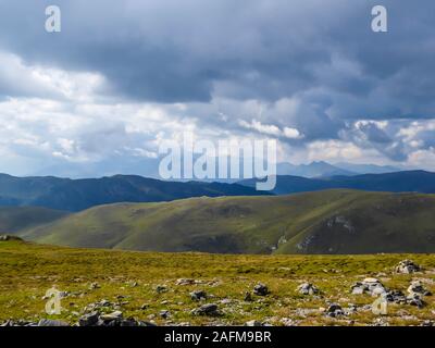 Des sentiers de randonnée dans la haute montagne. L'herbe verte, les buissons et les pierres sur les pentes. Chaînes sans fin des montagnes visibles. D'épais nuages sur le ciel. Sol Banque D'Images