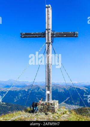 Une croix un t au sommet d'un pic de montagne. Une paire de bâton de randonnée et un sac à dos appuyé sur un pilier de la croix. Ciel bleu et clair. Chaînes sans fin Banque D'Images