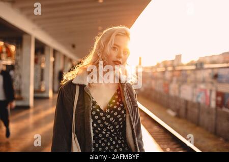 Jeune femme en attente de train à la station de métro au coucher du soleil Banque D'Images