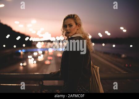 Jeune femme debout sur le pont dans la ville contre le ciel au coucher du soleil Banque D'Images