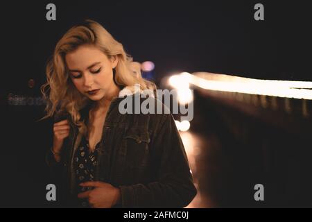 Portrait of young woman standing contre pont lumineux en ville