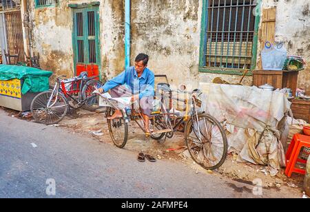 YANGON, MYANMAR - février 17, 2018 : Le vélo-taxi, lit le journal dans la rue sale minable de Chinatown, le 17 février à Yangon Banque D'Images