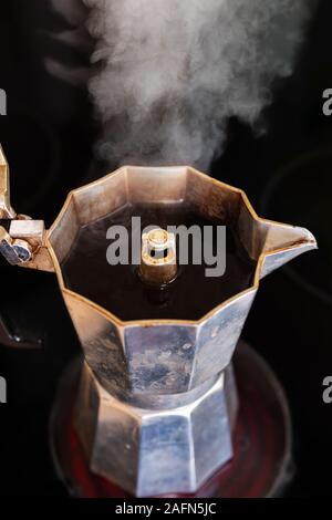 Café frais dans un pot de moka sur une plaque rouge avec la vapeur blanche s'élevant, close-up, portrait, format vertical Banque D'Images