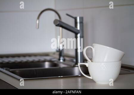 Deux tasses de thé blanc propre sur l'arrière-plan d'un métal lavabo avec un robinet d'eau potable et de robinet, robinet, selective focus Banque D'Images