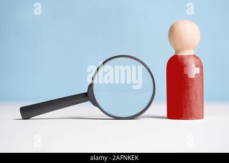 Le concept de contrôle, l'analyse de l'abstrait, médecin. Une figurine en bois en rouge à côté d'une loupe en verre. Close up. Banque D'Images