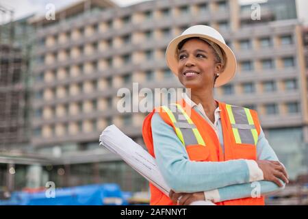 Fier jeune ingénieur femme tenant un rouleau de plans de bâtiment sur un chantier de construction. Banque D'Images