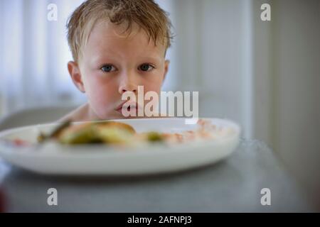 Jeune garçon est assis à une table avec un plateau de nourriture devant lui. Banque D'Images