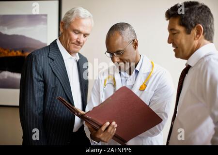 Trois médecins de discuter des dossiers de patient dans un couloir. Banque D'Images