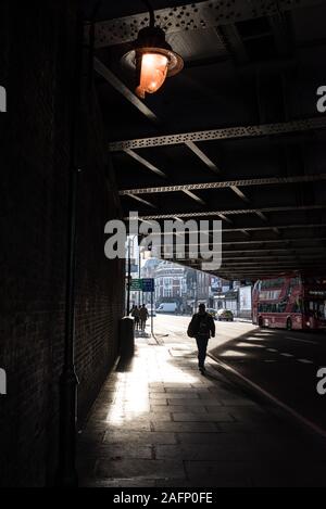 Scène de rue à Shoreditch, Londres est à l'ombre d'ossature d'une personne marche sous un pont routier et London bus rouge Banque D'Images