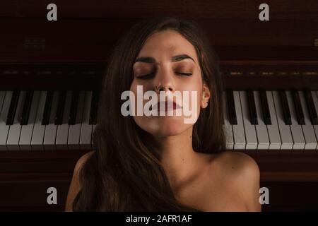 Belle femme à rêver la musique en face de piano Banque D'Images