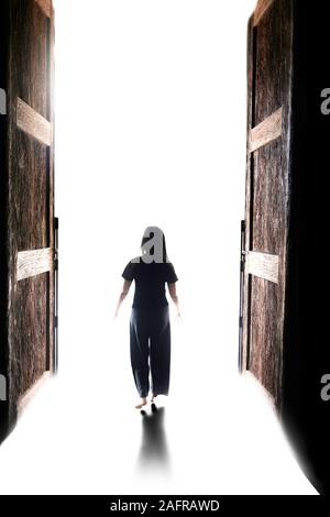 Femme marche dans la lumière à travers la porte grande ouverte Banque D'Images