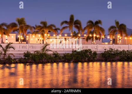 San Pedro, Ambergris Caye, Belize. Une vue d'un resort tropical avec des palmiers, ce qui reflète la lumière sur l'eau encore pendant l'heure bleue. Banque D'Images