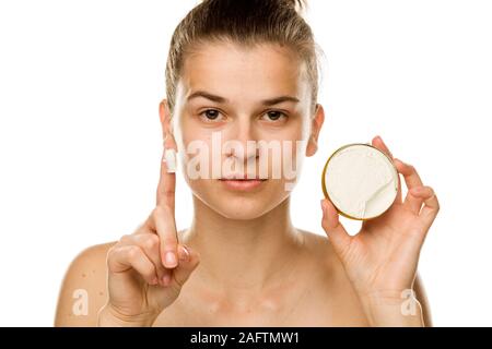 Portrait de jeune femme montrant la crème pour le visage avec son doigt sur fond blanc Banque D'Images