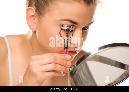 Jeune femme avec ses cils de curling le curling sur fond blanc Banque D'Images