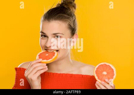 Young Beautiful woman eating tranches de pamplemousses sur fond jaune Banque D'Images