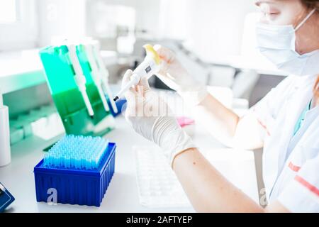 Femme Jeune scientifique dans un manteau blanc et un masque fonctionne en laboratoire médical ou biologique moderne pour la préparation de l'ADN. Banque D'Images