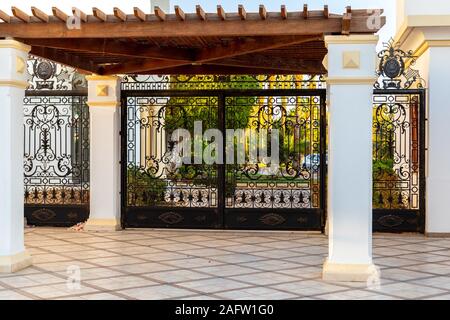 Belle porte et tropicale luxuriante verdure derrière. Colonnes et clôture en fer forgé. De riches boiseries entrée à motifs de luxe est verrouillée avec une chaîne. Banque D'Images