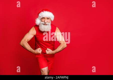 Portrait of cheerful sportsman dans hat montrant ses triceps portant des vêtements sports cap sur fond rouge isolé Banque D'Images