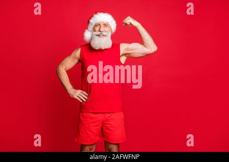 Portrait of cheerful santa claus à smiling montrant ses biceps portant des vêtements sports cap sur fond rouge isolé Banque D'Images