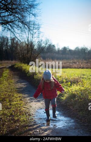 3 ans enfant s'éclabousser dans une flaque avec wellies sur une journée d'hiver ensoleillée. Tir vertical. Banque D'Images