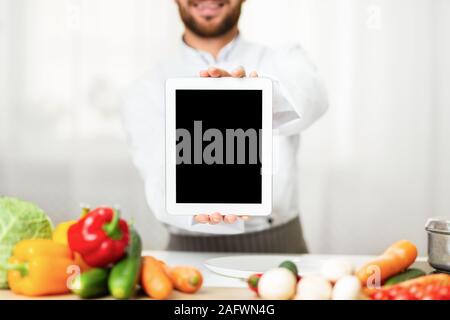 Chef Man Showing Tablet écran debout dans une cuisine de restaurant, Cropped Banque D'Images