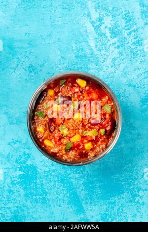 Chili con carne, un ragoût mexicain chaud avec du boeuf haché, haricots, maïs sucré, et le piment, tourné par le haut sur un fond bleu avec copyspace Banque D'Images